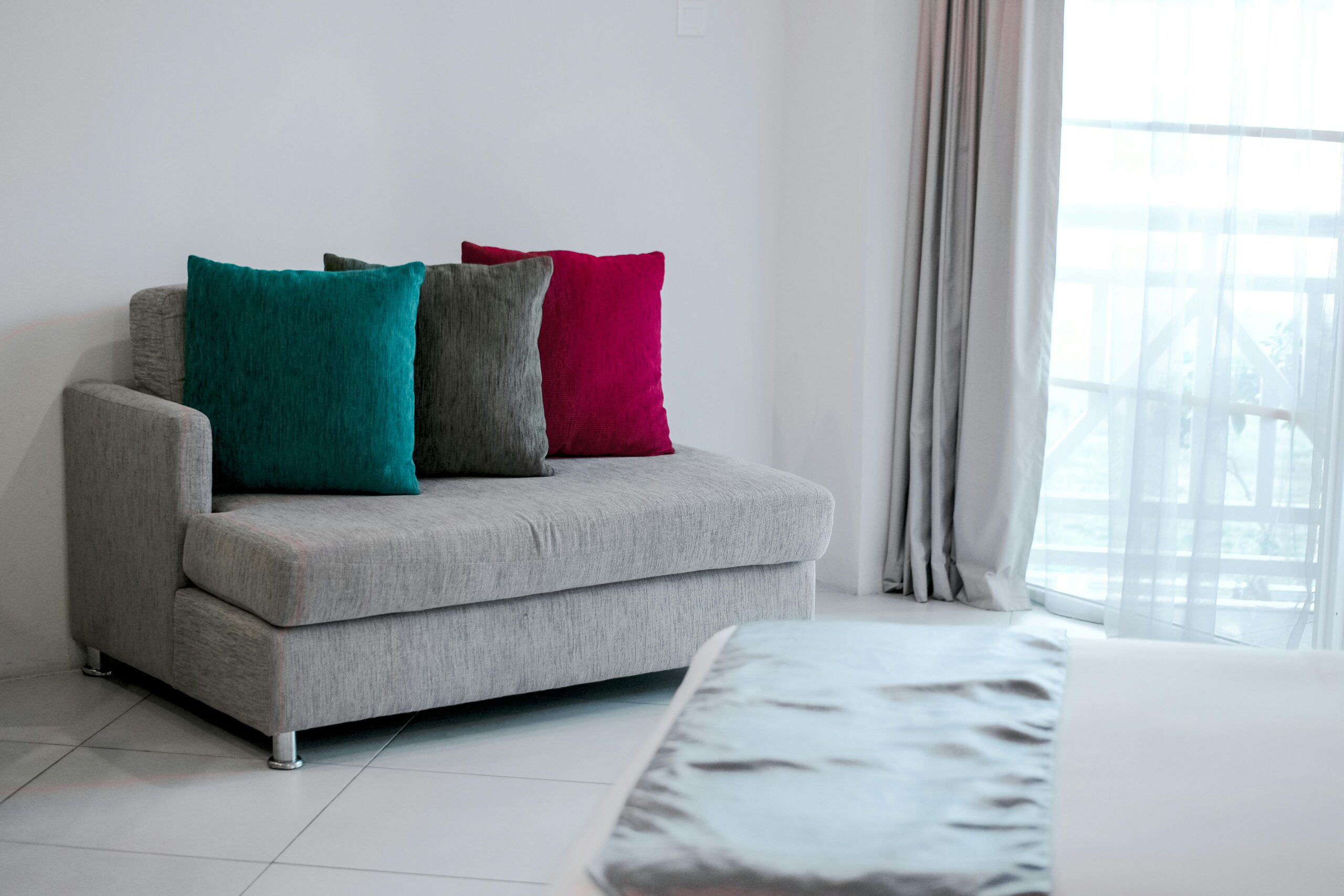 Simple modern interior featuring a grey sofa with vibrant colored cushions in a bright room.